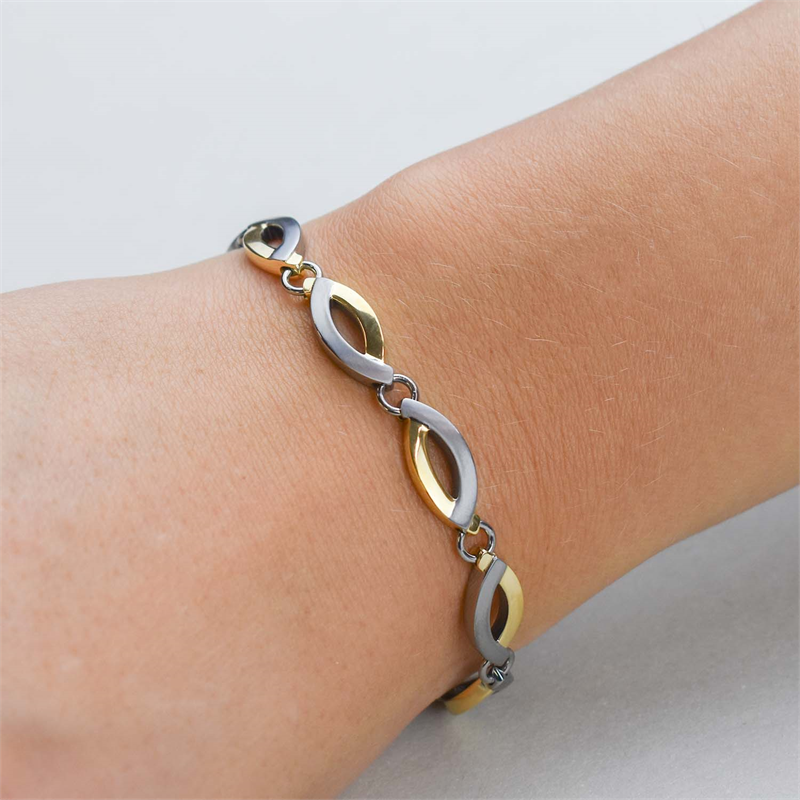 Een close-up van een pols met de Boccia Titanium Armband Bicolor 03001-02, met afwisselend gouden en zilveren ovale titanium schakels van Boccia, tegen een lichte, neutrale achtergrond.