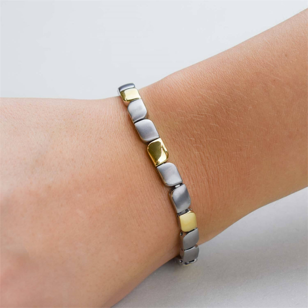 Een close-up van een pols met de Boccia Titanium Armband Bicolor 03007-02 van Boccia, met afwisselend zilveren en gouden rechthoekige schakels tegen een effen, lichte achtergrond.