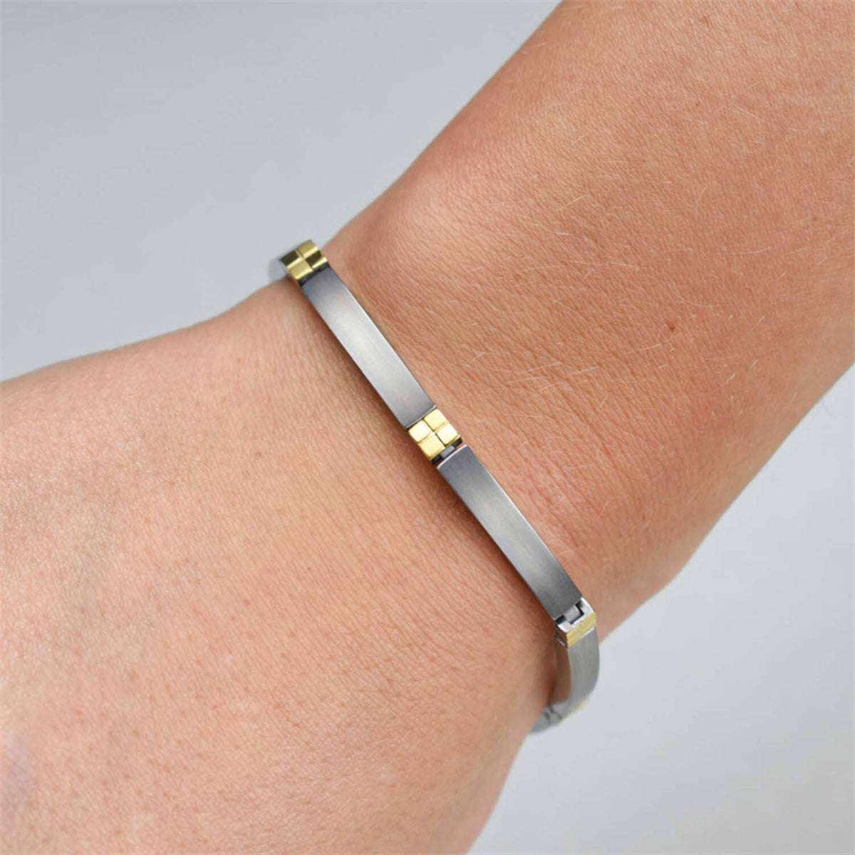 Een close-up toont een pols met de Boccia Titanium Armband Bicolor 0329-04, met drie gouden accenten op een strakke zilveren band, tegen een lichtgrijze achtergrond.
