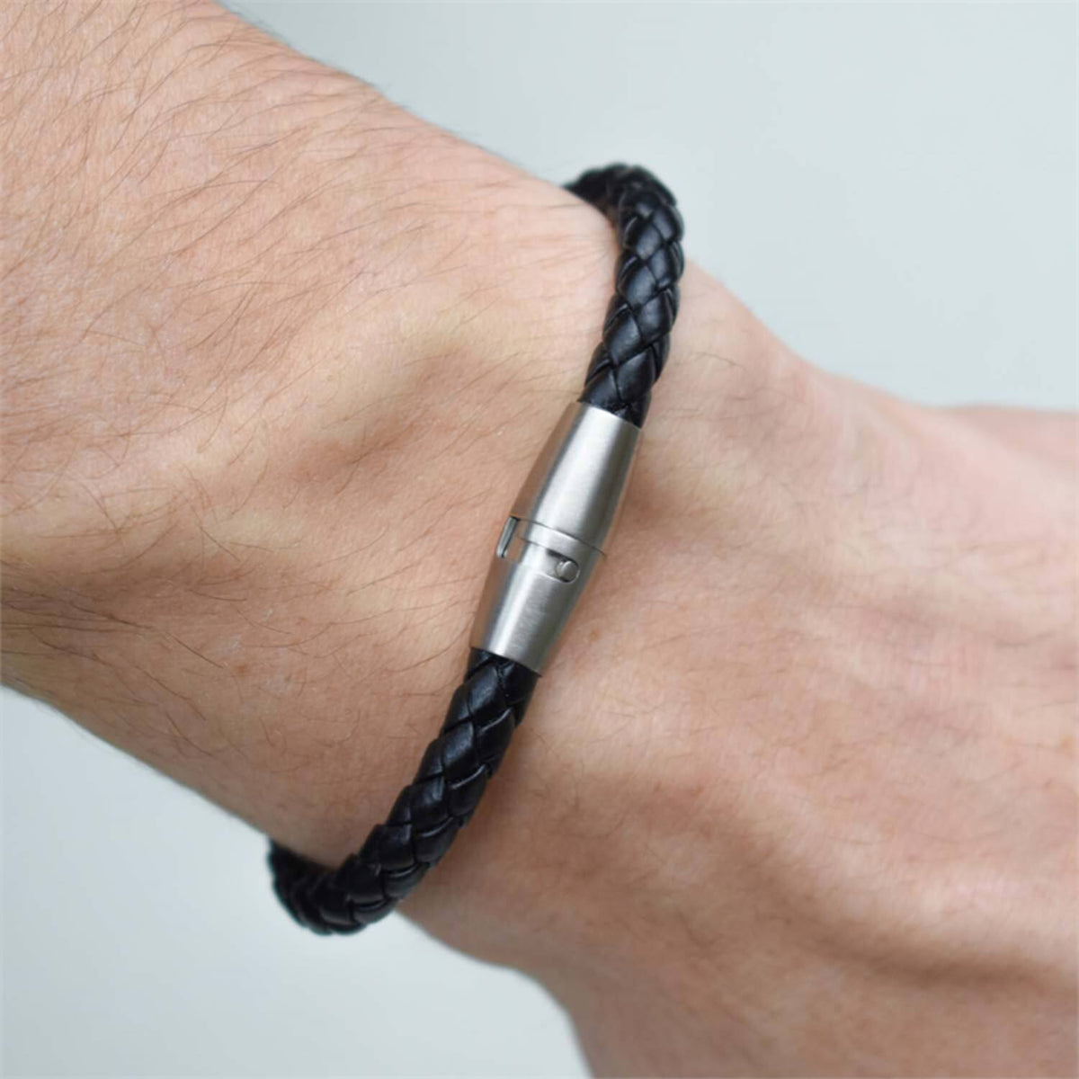 Een close-up van een pols die de Boccia Titanium Armband leer 0347-01 draagt, een zwart gevlochten leren armband met een zilveren magnetische sluiting van Boccia, tegen een effen lichte achtergrond.