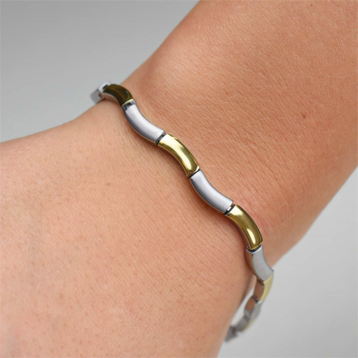 Close-up van een pols met de Boccia Titanium Armband Bicolor 0370-02, met afwisselend gouden en zilveren metalen schakels in een golvend, modern ontwerp tegen een neutrale achtergrond.