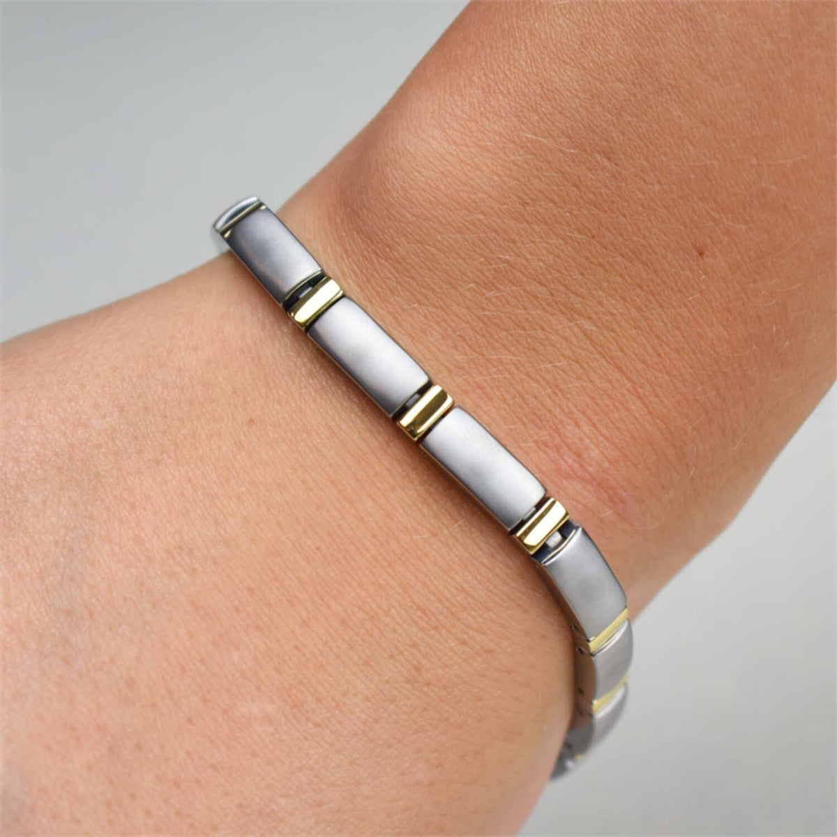 Een close-up toont een Boccia Titanium Armband Bicolor 0371-02 met strakke, zilverkleurige, rechthoekige schakels en subtiele gouden accenten, die het kenmerkende tweekleurige ontwerp van het merk benadrukken.
