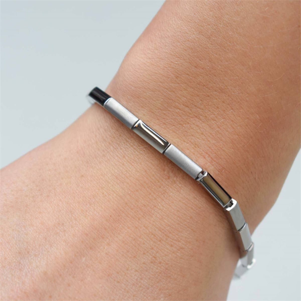 Een close-up toont de pols van een persoon, versierd met de Boccia Titanium Armband 0387-01, met een minimalistisch ontwerp met rechthoekige schakels, tegen een effen, lichte achtergrond.