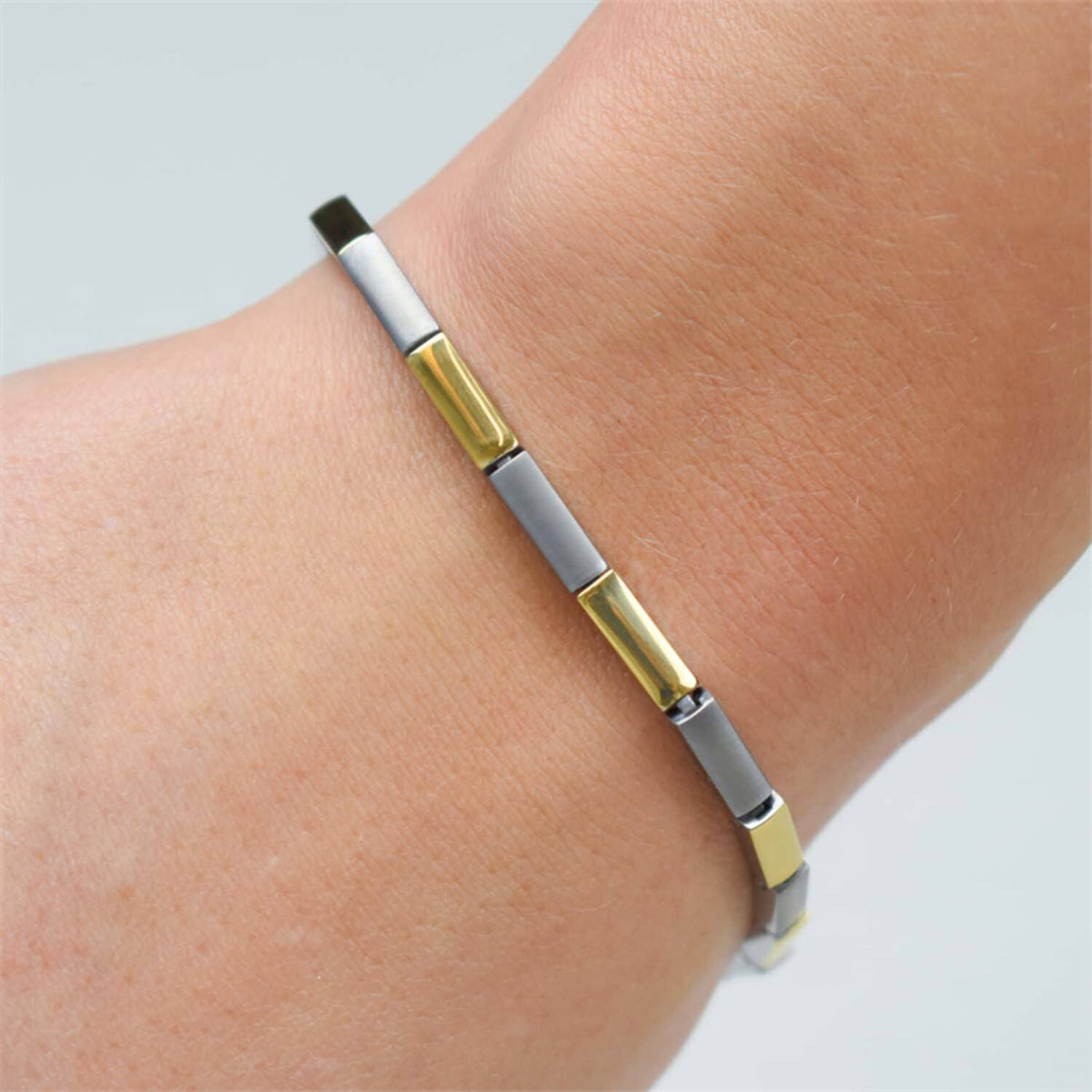 Een close-up van een pols met de Boccia Titanium Armband Bicolor 0387-02 van Boccia, met afwisselend gouden en zilveren rechthoekige schakels voor een strakke, moderne look.