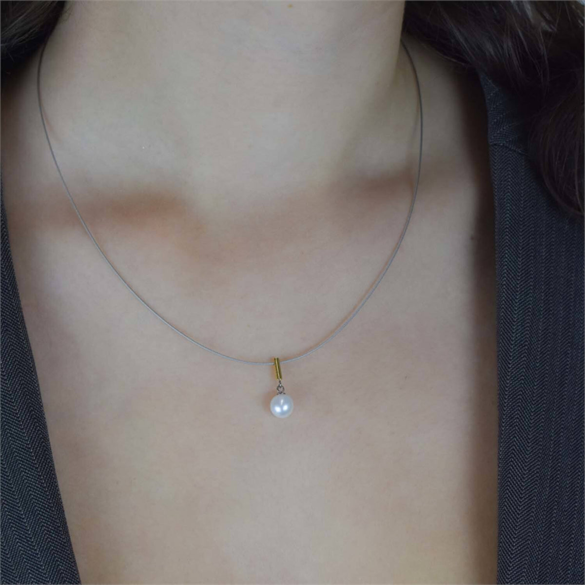Een close-up van een persoon die de Boccia Titanium Collier Parel Bico st 08036-02 draagt: een slanke ketting met een enkele witte parel als hanger, stijlvol gecombineerd met een donker topje met V-hals.