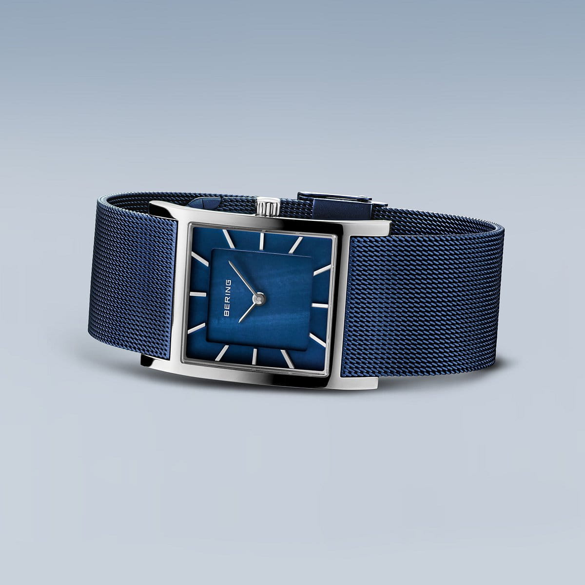 Het Bering dameshorloge model 10426-307-S heeft een rechthoekige blauwe wijzerplaat met een zilveren frame en mesh band. Het heeft zilveren uurmarkeringen en twee wijzers op een gradiëntblauwe achtergrond onder saffierglas, wat een minimalistisch ontwerp vertoont.