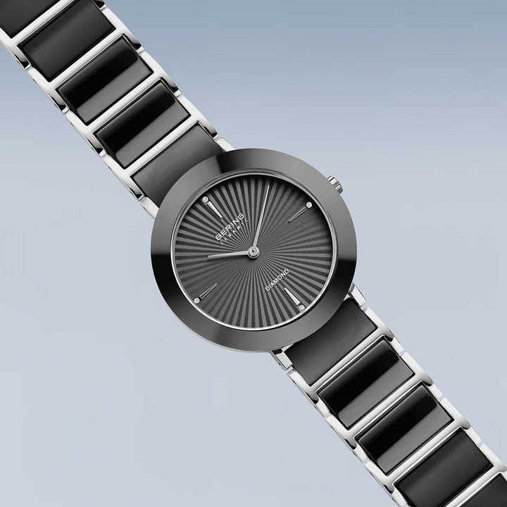 De Bering 11435-702 is een gestroomlijnd dameshorloge met een zwarte en zilveren metalen band en een ronde grijze wijzerplaat met stralende lijnen, zilveren uurmarkeringen en het Bering-logo bovenaan-een luxe horloge voor elke gelegenheid.