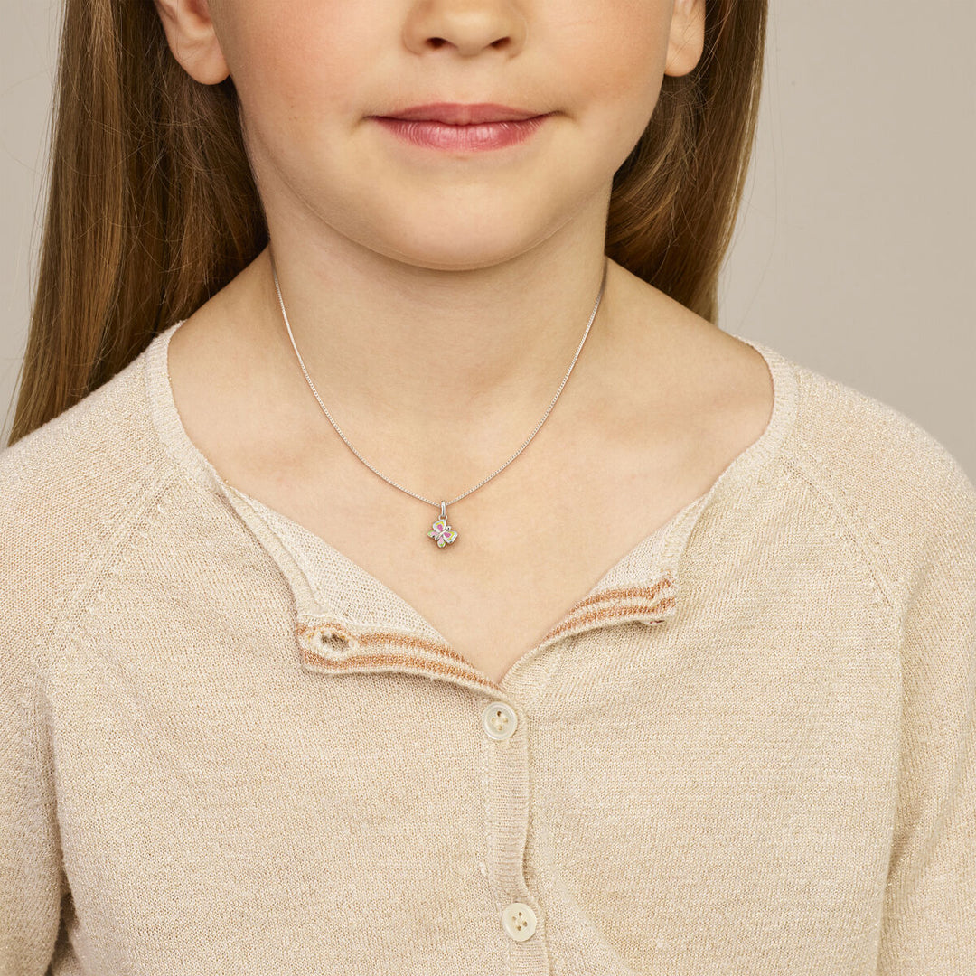 Een jong meisje draagt een beige vest en een Van der Kooij Collectie hanger vlinder zilver gerhodineerd, zachtjes glimlachend. Het beeld is cropped van schouders tot kin en is ideaal voor kinderen vrouwen.