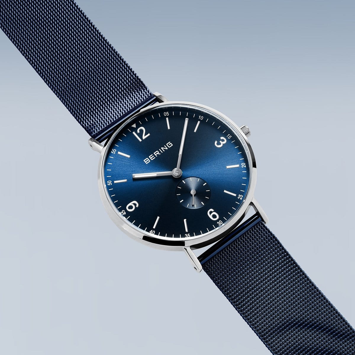 Het Bering heren horloge blauw 14040-307 is een minimalistisch herenhorloge met een blauwe mesh band, blauwe wijzerplaat, zilverkleurige uurmarkeringen, kleine secondewijzer en een quartz uurwerk van Bering tegen een lichtblauwe achtergrond.