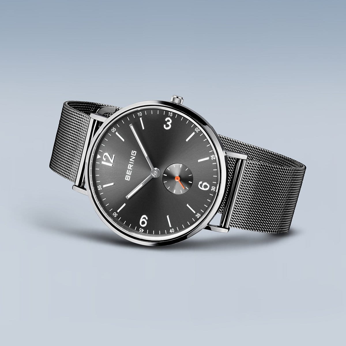 De Bering heren horloge grijs 14040-377 heeft een gestroomlijnd zilverkleurig ontwerp, een zwarte wijzerplaat met minimalistische witte markeringen, een fijnmazige band en een elegant kwartsuurwerk - afgebeeld tegen een blauwgrijze achtergrond met kleurverloop.