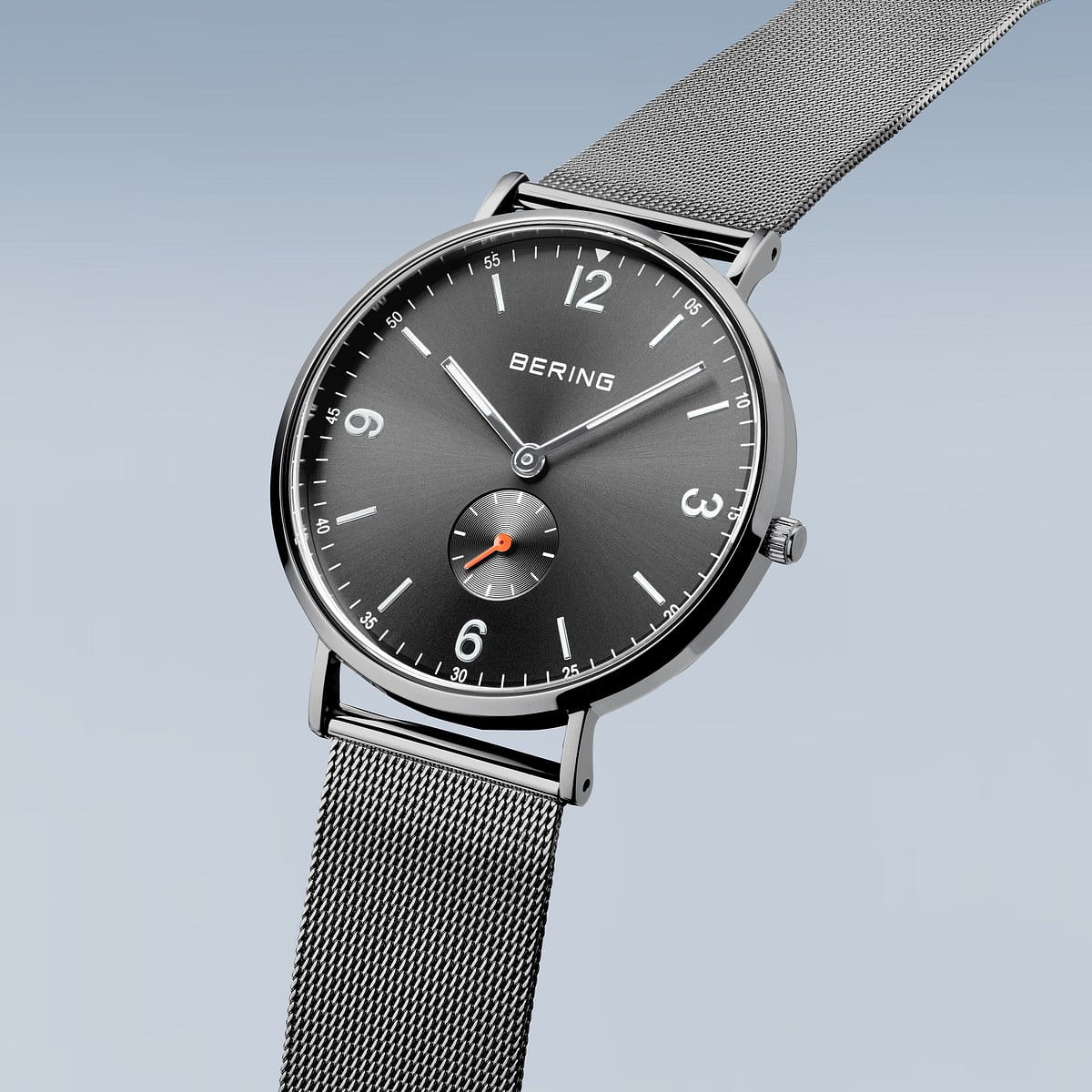 Het Bering heren horloge grijs 14040-377, een minimalistisch roestvrijstalen horloge met zwarte wijzerplaat, zilverkleurige uurmarkeringen, mesh band en kleine secondewijzer op 6 uur, wordt getoond tegen een lichtgrijze achtergrond. Merk: Bering.