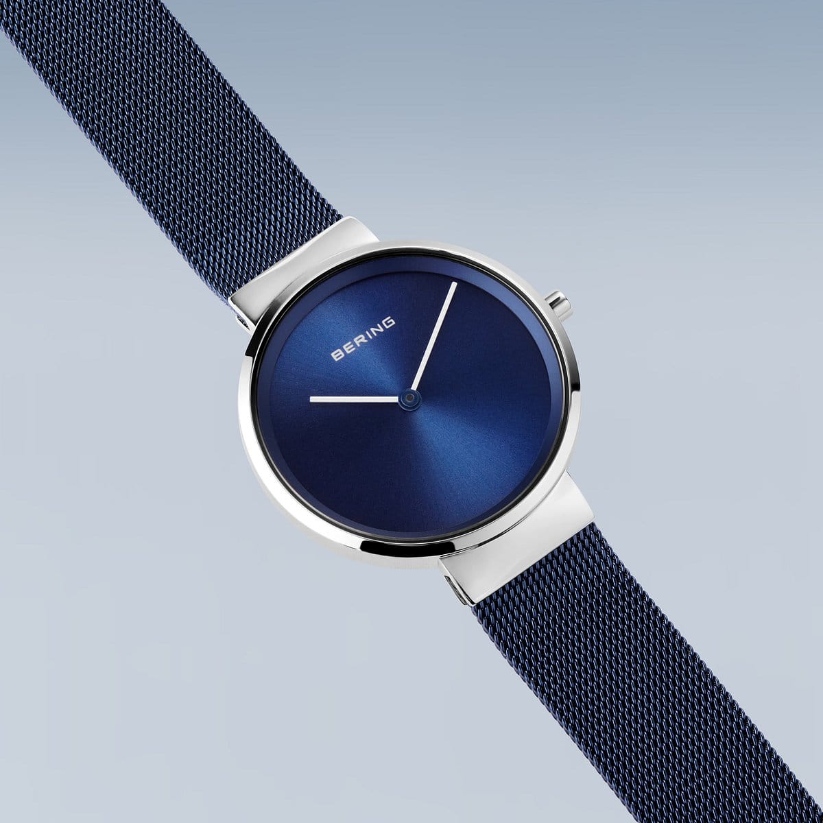 De Bering 14531-307 is een slank blauw polshorloge met een glanzende wijzerplaat en een minimalistisch ontwerp met Quartz-uurwerk. Het heeft zilverkleurige wijzers, een ronde roestvrijstalen kast en een blauwe meshband. Het merk Bering verschijnt op de wijzerplaat tegen een lichtblauwe achtergrond met kleurverloop.
