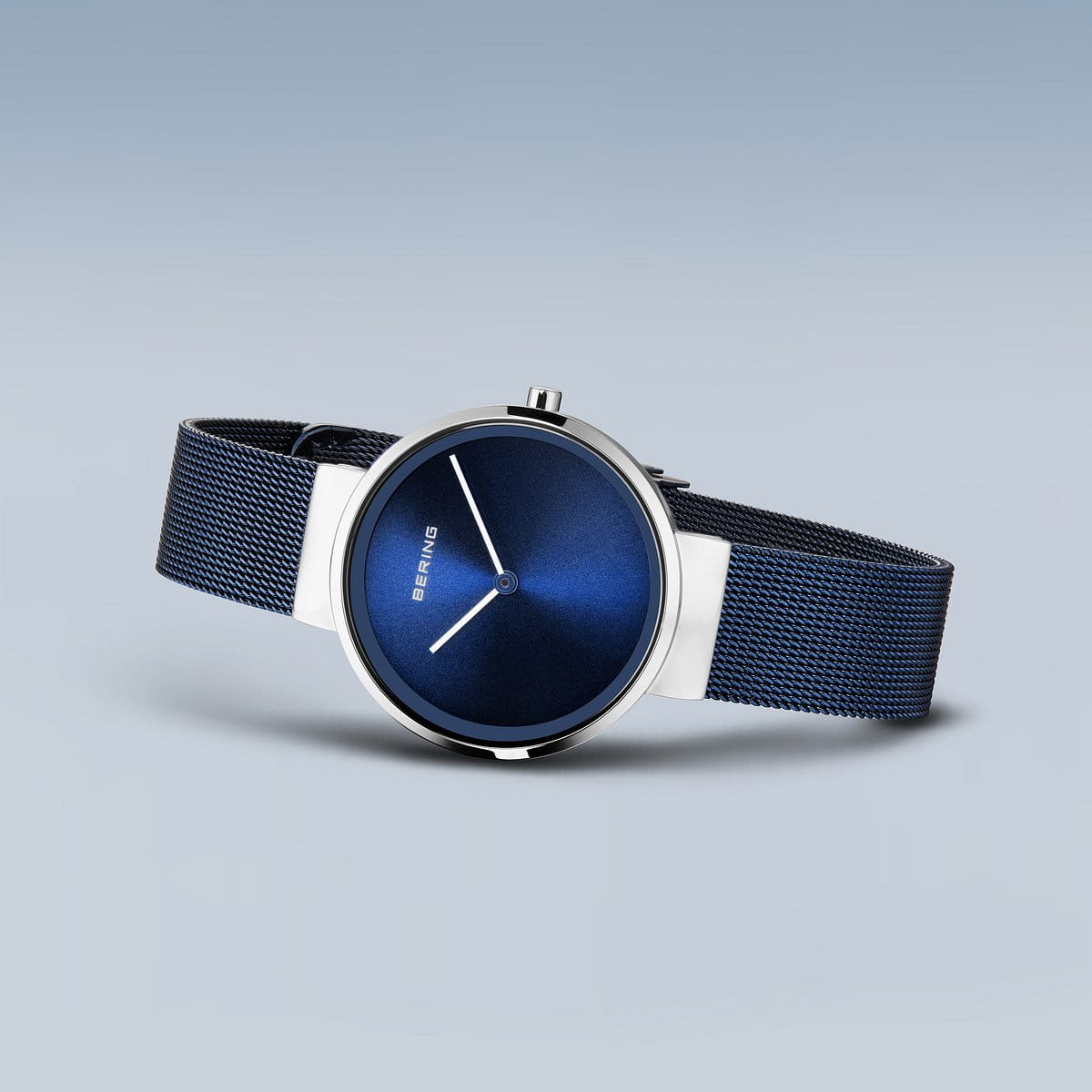 De Bering 14531-307 is een strak dameshorloge met een diepblauwe wijzerplaat en zilveren wijzers, wat een minimalistisch design laat zien. Gemaakt van roestvrij staal, heeft het een bijpassende blauwe meshband tegen een zachtgrijze achtergrond.