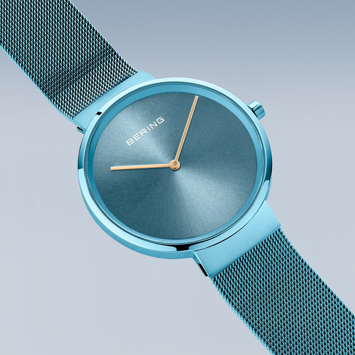 De Bering 14539-388, een strak turquoise horloge met een mesh band, staat op een gradiëntblauwe achtergrond. De minimalistische wijzerplaat heeft gouden uur- en minutenwijzers onder Saffierglas. BERING staat op de 12-uurspositie en toont Quartz-uurwerk precisie.