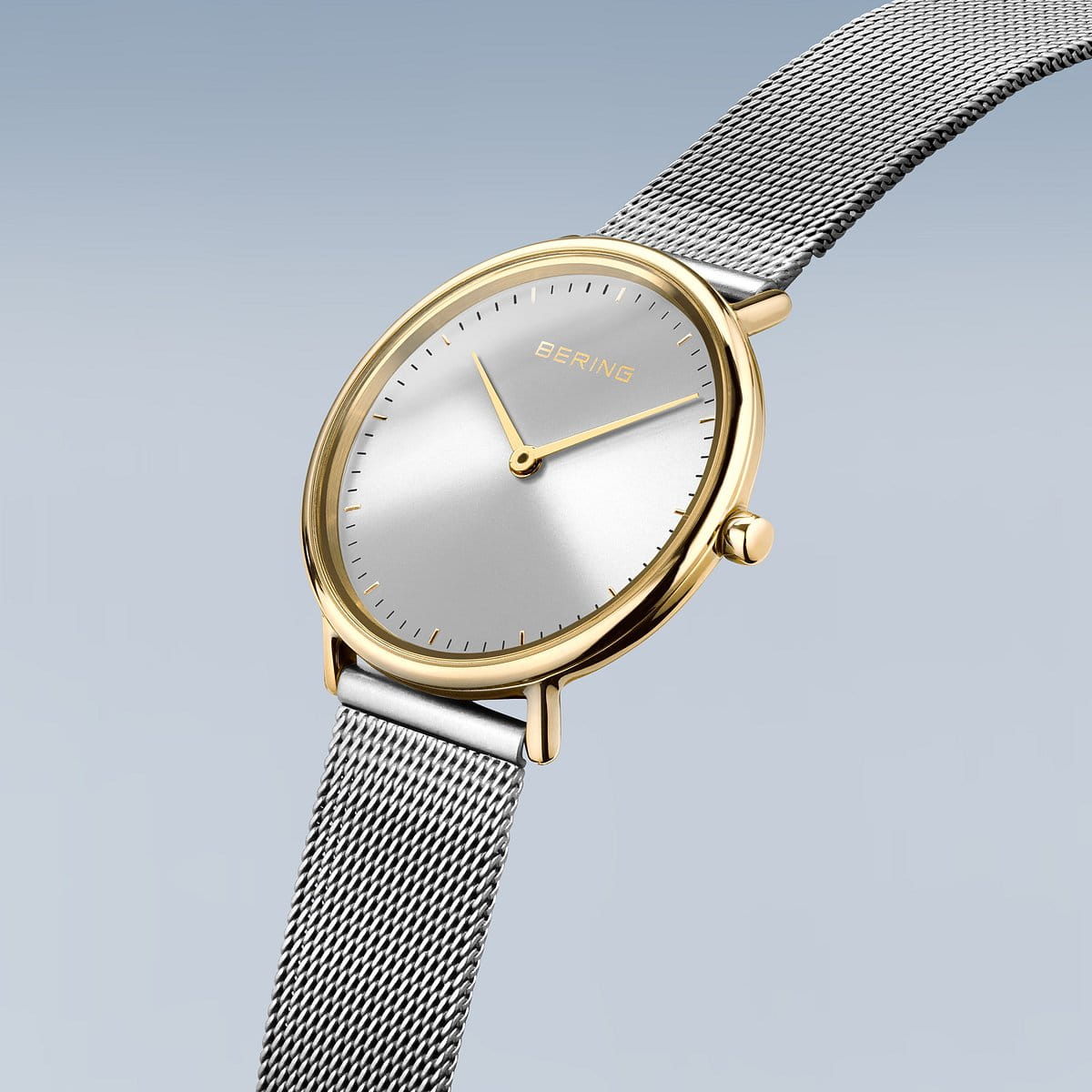 De Bering 15729-010 is een strak dameshorloge met een minimalistische zilveren wijzerplaat, gouden wijzers en roestvrijstalen kast. Het heeft een mesh zilveren band en Bering opschrift op de wijzerplaat tegen een zachtblauwe gradiëntachtergrond, wat de tijdloze Quartz-technologie belichaamt.