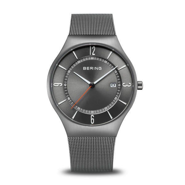 Grijs horloge met een mesh-band, ronde wijzerplaat en oranje secondewijzer.