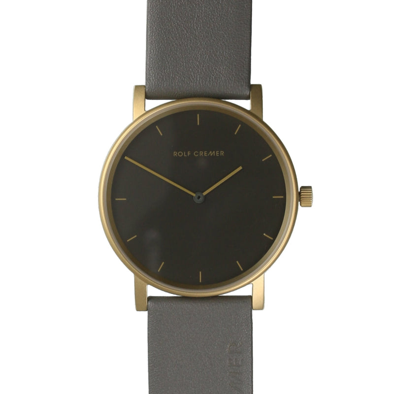 Gouden horloge met een grijze leren band en een donkere wijzerplaat zonder cijfers.