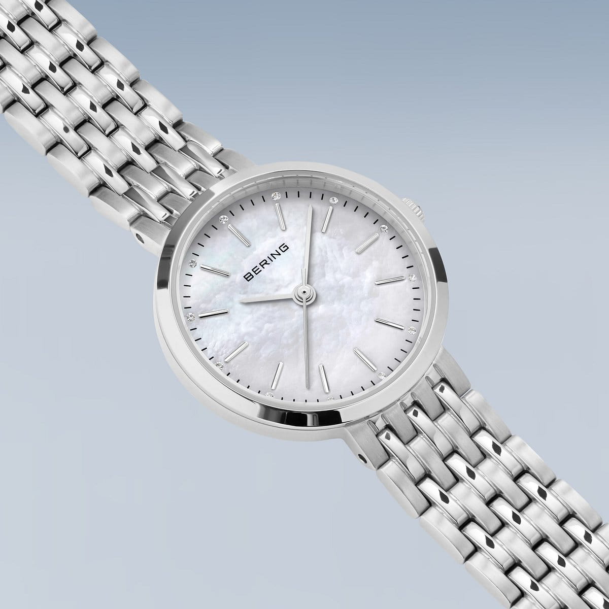 Een close-up van de Bering dames horloge parelmoer wijzerplaat - 19126-700, met een zilveren kast, witte parelmoer wijzerplaat, zilveren markers, metalen schakelband en quartz uurwerk van Bering, tegen een lichtblauwe achtergrond.