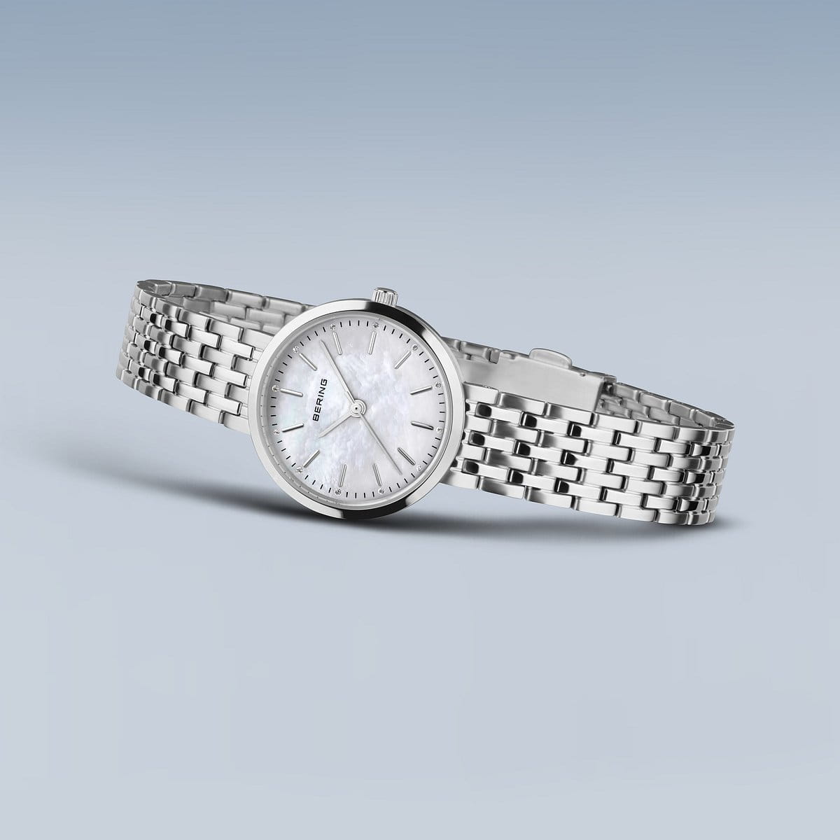 De Bering dames horloge parelmoer wijzerplaat (19126-700) heeft een zilverkleurige metalen band, ronde witte parelmoer wijzerplaat, minimalistische uurmarkeringen en quartz uurwerk, weergegeven op een lichtblauwe gradiënt achtergrond.