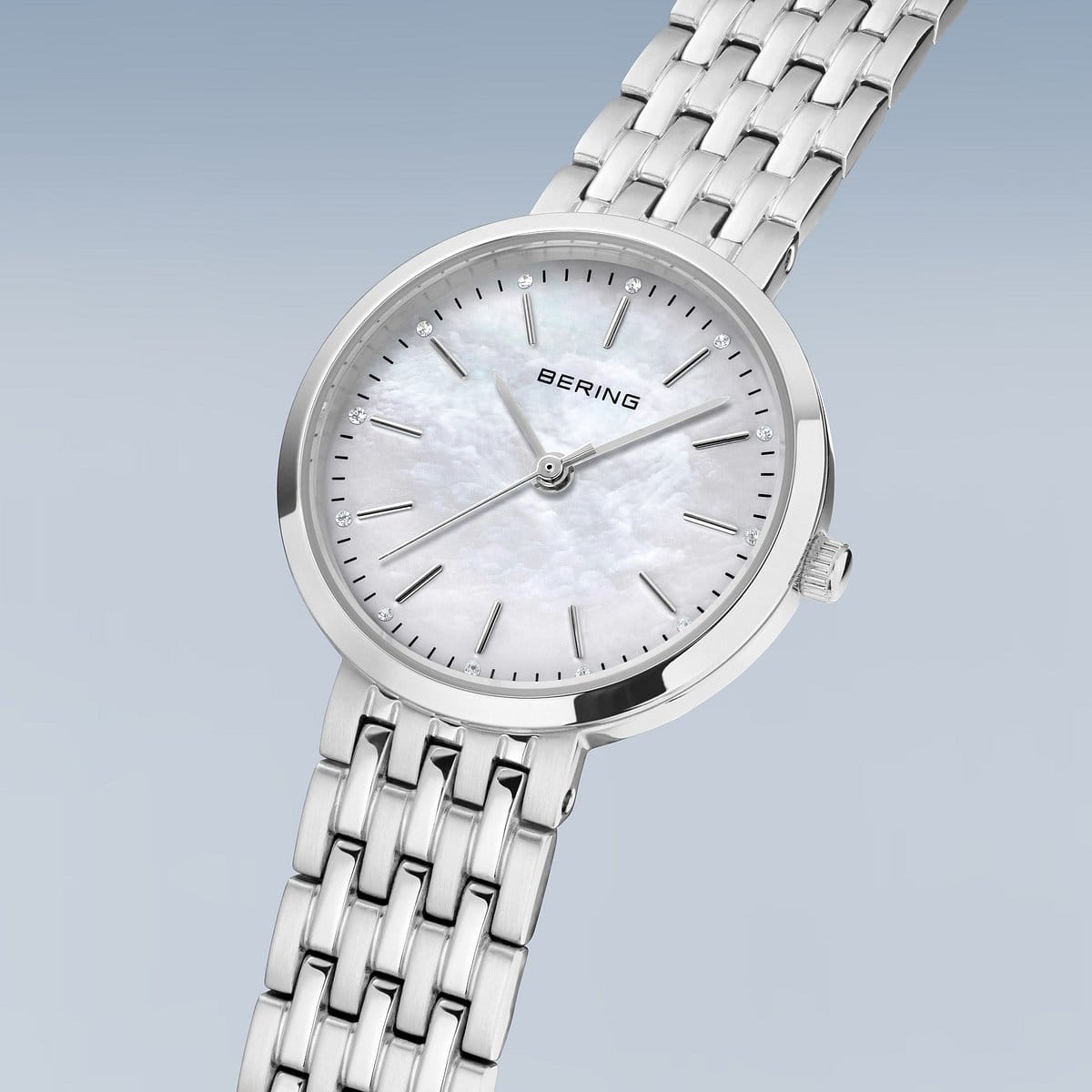 Het Bering dames horloge 19126-700 heeft een zilverkleurige metalen schakelband, minimalistische uurmarkeringen en een witte parelmoer wijzerplaat met quartz uurwerk, afgebeeld tegen een lichtblauwe achtergrond.