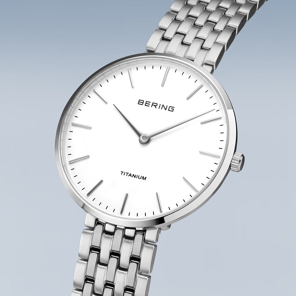 Het Bering dames horloge witte dial - 19334-004 is een strak horloge met een minimalistisch design met een ronde, witte wijzerplaat, eenvoudige uurmarkeringen, slanke wijzers op een lichtblauwe saffierglas achtergrond met kleurverloop en een zilveren titanium band.