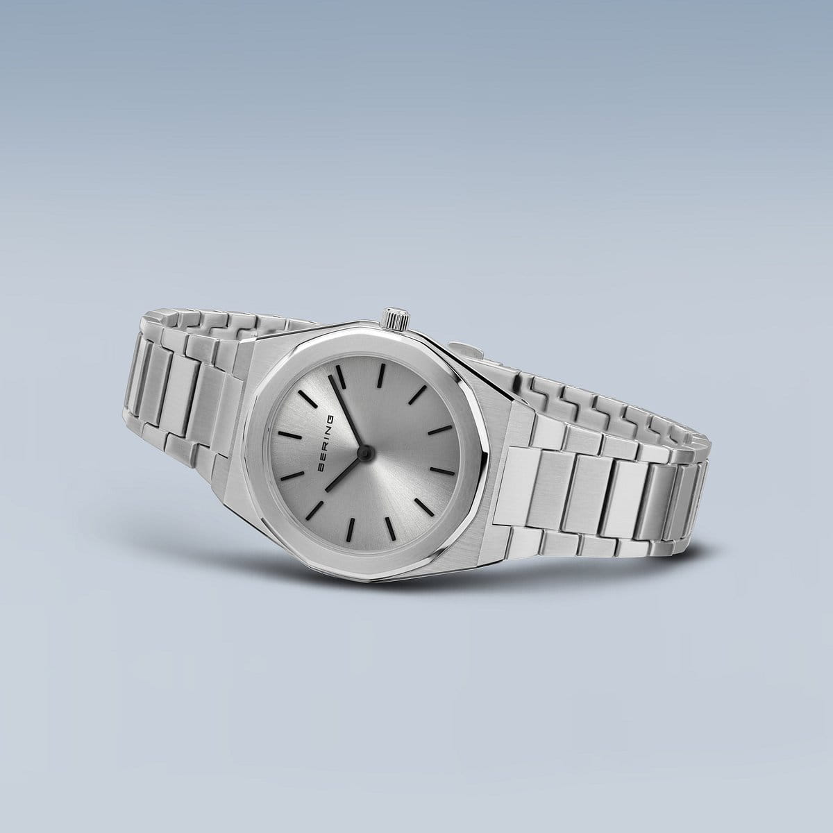 Het Bering dames horloge zilveren dial - 19632-700 heeft een strak zilveren design met een metalen band, minimalistische ronde wijzerplaat, eenvoudige zwarte wijzers en een kleine kroon. Het heeft een nauwkeurig quartz uurwerk en een zachte gradiënt lichtblauwgrijze achtergrond.