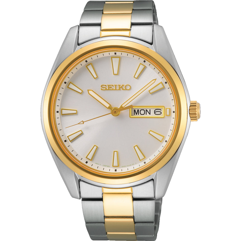Het Seiko heren horloge SUR446P1 heeft een zilveren en gouden metalen band met een ronde wijzerplaat, gouden uurmarkeringen en wijzers. Het heeft een dag-/datumweergave aan de rechterkant, een gouden lunette en duurzaam saffierglas, wat elegantie en duurzaamheid combineert.