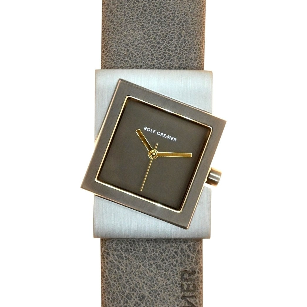 Vierkant Rolf Cremer horloge met grijze wijzerplaat, gouden wijzers en een leren band in lichtgrijs.