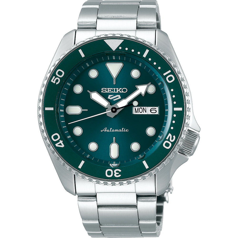 Het Seiko 5 Sports heren horloge SRPD61K1 is een opvallend automatisch polshorloge met een zilveren metalen band, groene wijzerplaat, lichtgevende uurmarkeringen, dag-datumweergave en draaibare lunette gemarkeerd 10-50. Dit Seiko-model geeft de tijd elegant weer op 10:08.