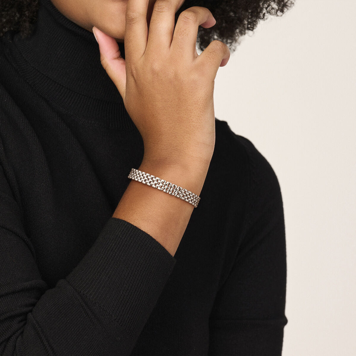 Een persoon in een zwarte coltrui toont een Van der Kooij Collectie armbandpanter 8 mm 17 cm zilver gerhodineerd om zijn pols, terwijl hij zijn hand bij zijn gezicht houdt tegen een effen, neutrale achtergrond.