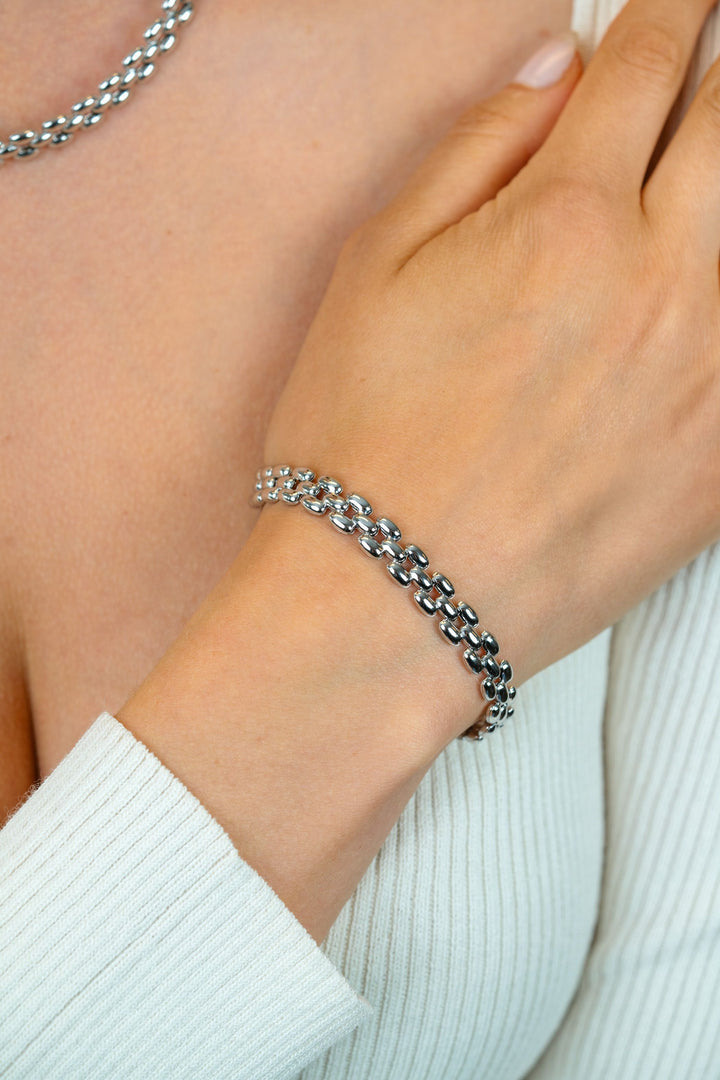 Een persoon in een witte geribbelde top showt de Zinzi Armband zilver ZIA2764 en bijpassende ketting. Hun hand op hun borst vestigt de aandacht op de elegante glans van de zilveren sieraden van Zinzi tegen hun lichte huid.