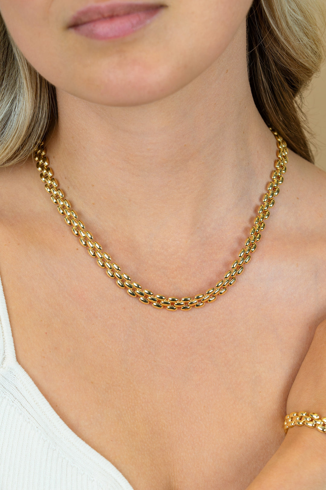 Een vrouw met een lichte huidskleur, gekleed in een wit topje, draagt de Zinzi Ketting Gold Plated ZIC2764G ketting van Zinzi en een bijpassende gouden armband. Afgebeeld vanaf de schouders omhoog.