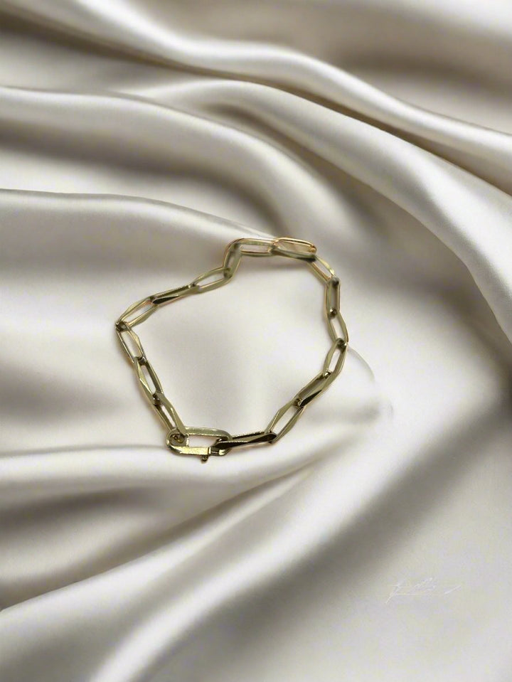 De vintage gouden armband 14k closed forever van Juwelier van der Kooij rust elegant op luxueus wit satijn, waarbij de langwerpige gouden schakels prachtige contrasten in textuur en kleur creëren.