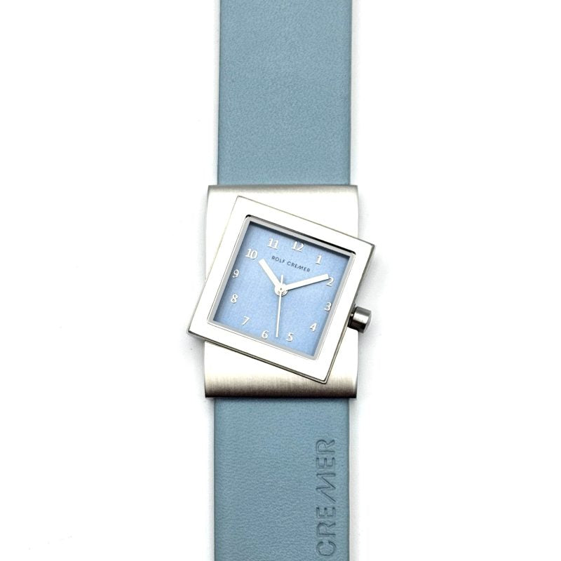 Vierkant Rolf Cremer horloge met lichtblauwe wijzerplaat en zilverkleurige kast, afgewerkt met een lichtblauwe rubberen band.