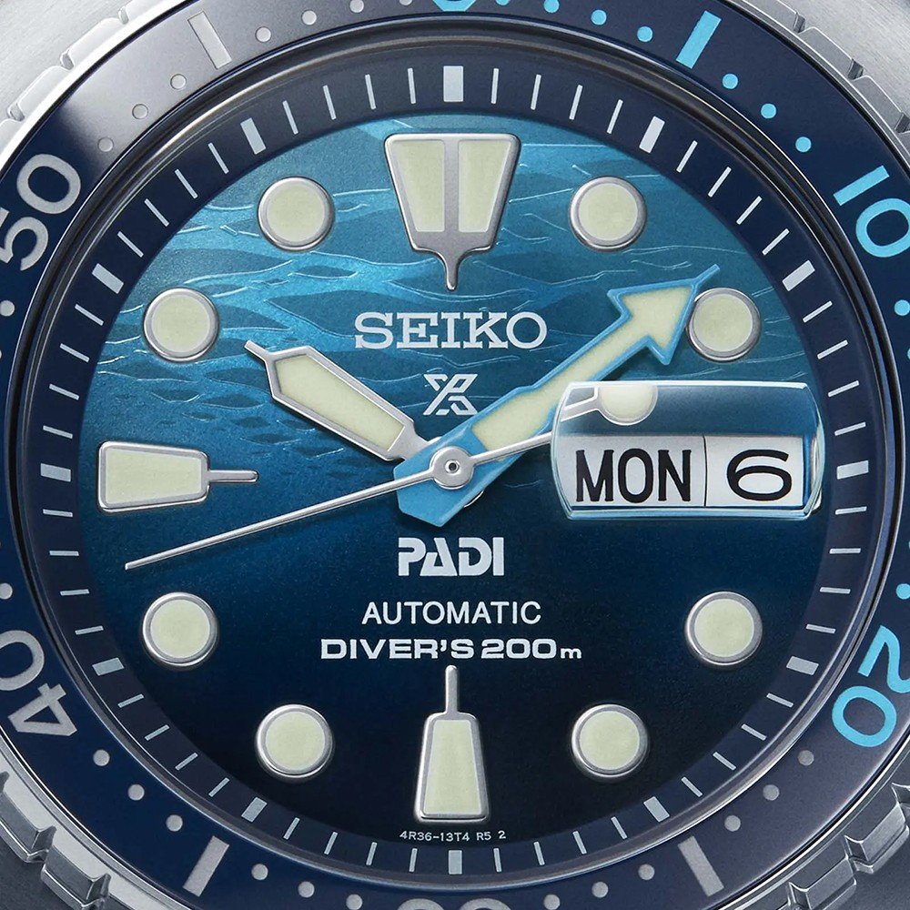Close-up van een Seiko Prospex herenhorloge SRPK01K1 met een blauwe wijzerplaat met lichtgevende markeringen, dag/datum en de teksten SEIKO, PADI en AUTOMATIC DIVERS 200m. Dit duikhorloge heeft een automatisch uurwerk en minutenmarkeringen op de lunette.