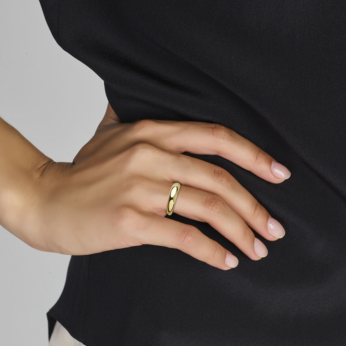 Een hand met keurig verzorgde nagels draagt de Van der Kooij Collectie ring 14K geelgoud met een ovaal ontwerp – een elegant damessieraad – rustend op zwarte stof.