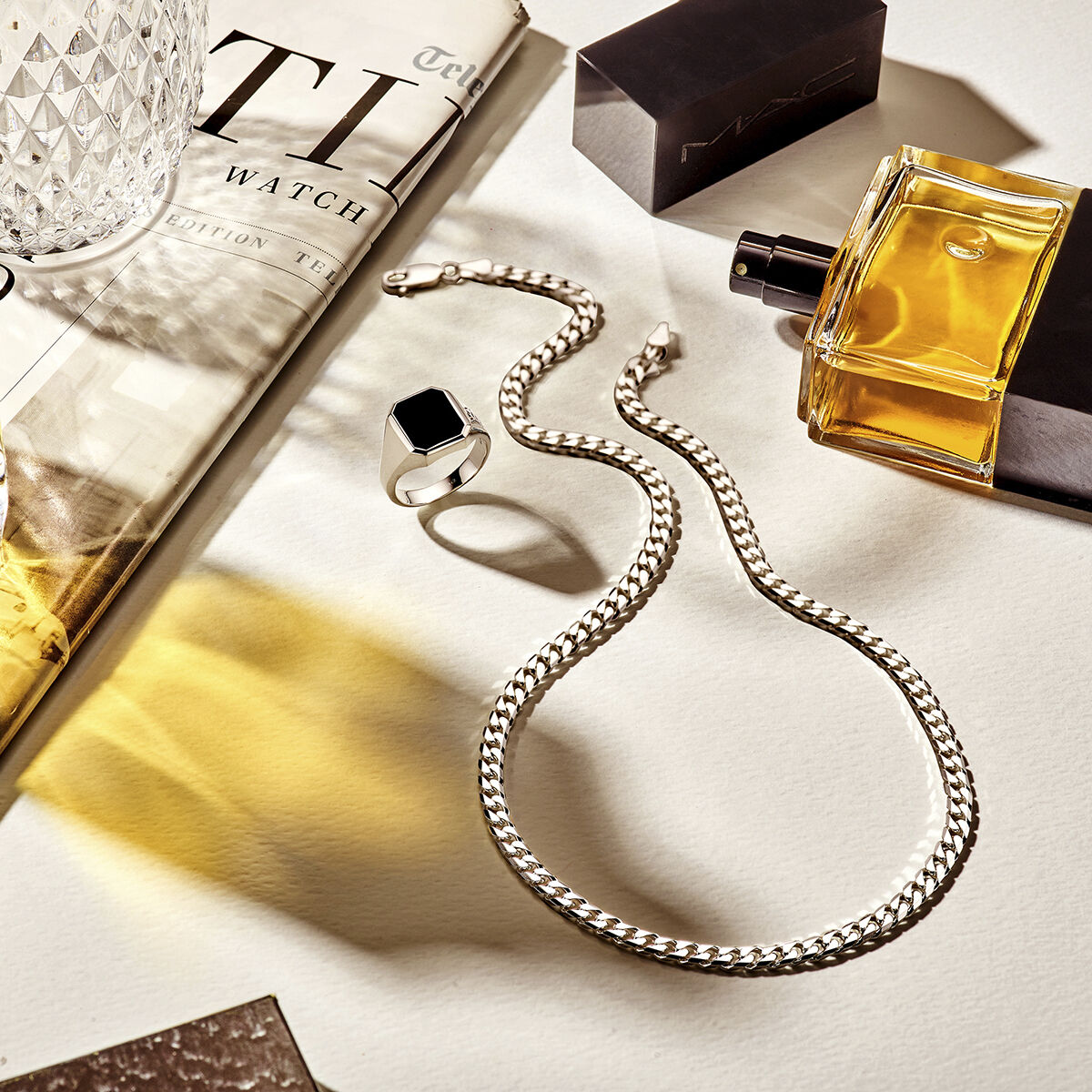 De zegelring massief onyx 13 x 11mm zilver gerhodineerd uit de Van der Kooij Collectie, een zilveren ketting, een parfumflesje, glas en magazine liggen stijlvol op een lichte ondergrond met zachte schaduwen.