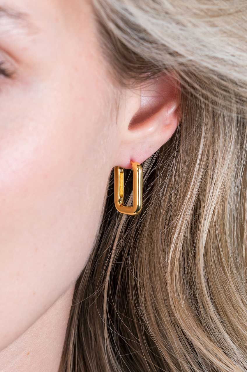 Close-up van een persoon met steil blond haar die glanzende rechthoekige gouden oorbellen draagt-Zinzi Oorbellen Gold Plated Zio2221 G van Zinzi.