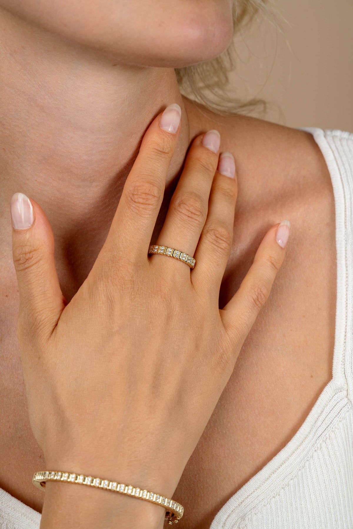 Een close-up toont de natuurlijke nagels en hand van een vrouw die de Zinzi Ring Zilver ZIR2686Y en een bijpassende gouden armband draagt. Ze legt haar hand op haar borst over een wit mouwloos topje.