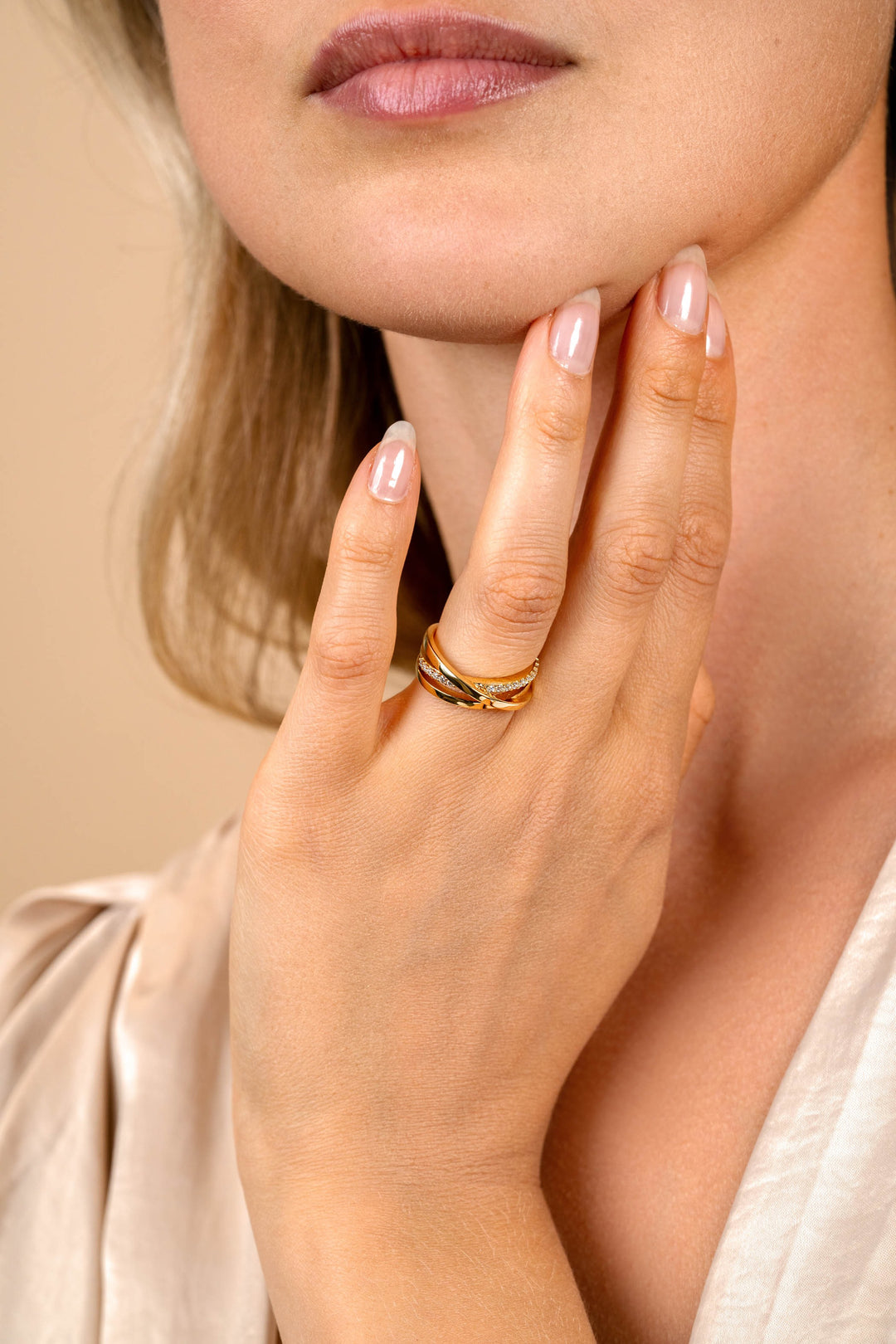 Een vrouw met een lichte huid raakt haar kin aan en toont de Zinzi Ring Gold Plated ZIR1774Y om haar vinger. Haar nagels zijn bleek en netjes en ze draagt een crèmekleurige zijden blouse van Zinzi. Haar lippen zijn lichtjes gespleten.