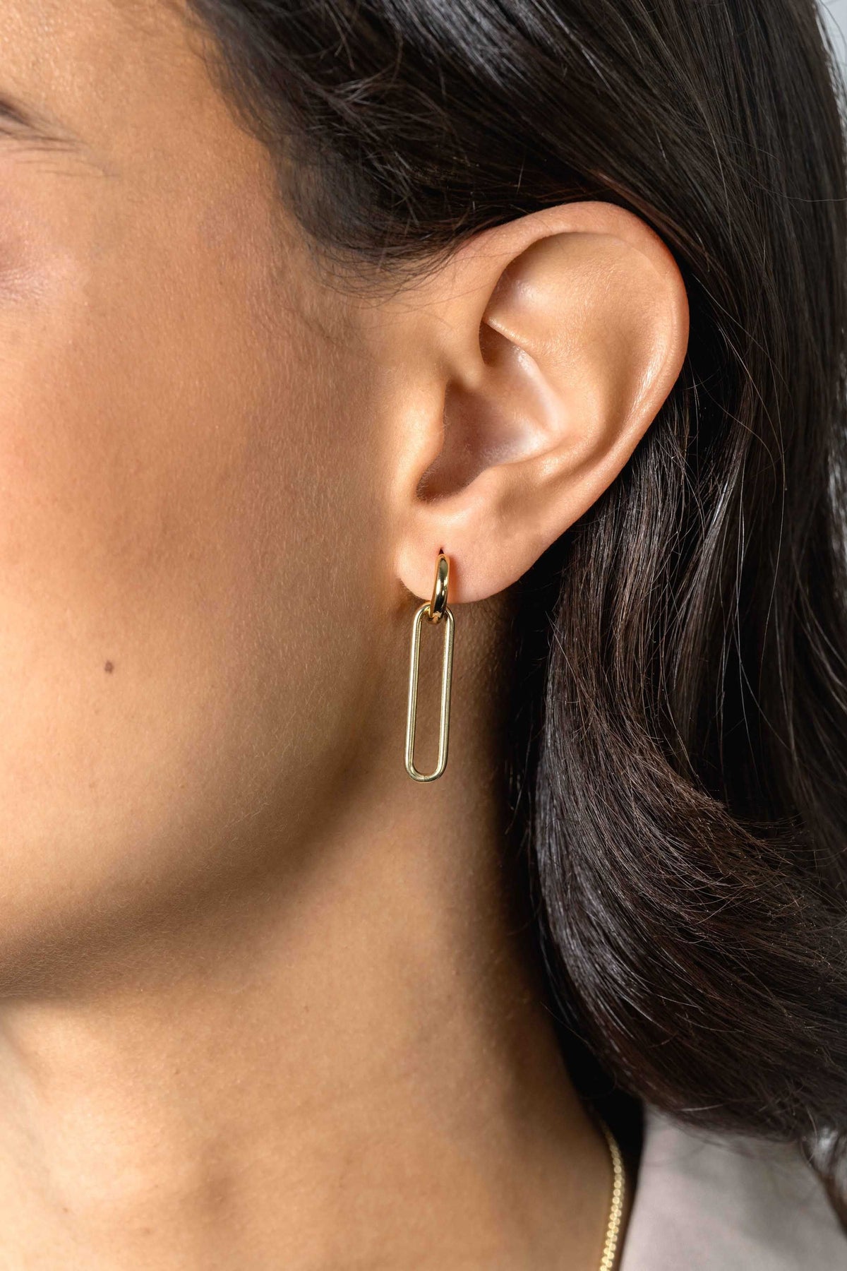 Close-up van het oor van een persoon die Zinzi Oorbedels Gold Plated Zich2416 G van Zinzi draagt. De eenvoudige rechthoekige oorbel accentueert de elegante ovale vorm en past bij de medium huid en het donkere, golvende haar.