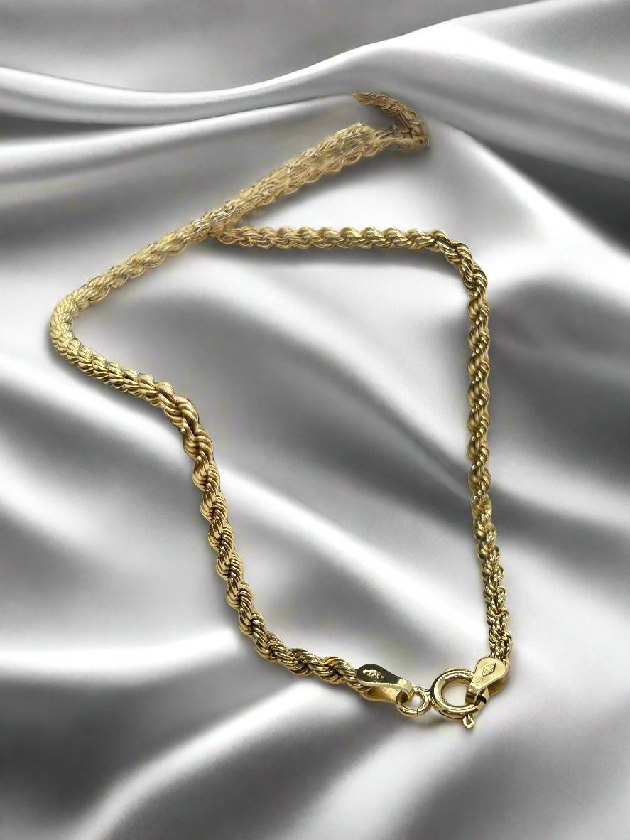 Het 14K vintage gouden collier van Juwelier van der Kooij, voorzien van een karabijnsluiting, is elegant gezet op gladde zilveren satijnen stof en belichaamt de tijdloze charme van onze Vintage Collectie sieraden.