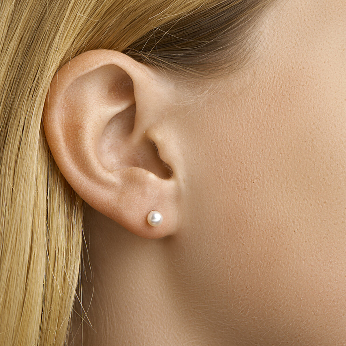 Close-up van het oor van een vrouw met steil blond haar, gekleed in Van der Kooij Collectie oorknoppen van parelmoer in 14 karaat geelgoud. De gladde huid accentueert de kleine, ronde witte parel in het midden van haar oorlel.