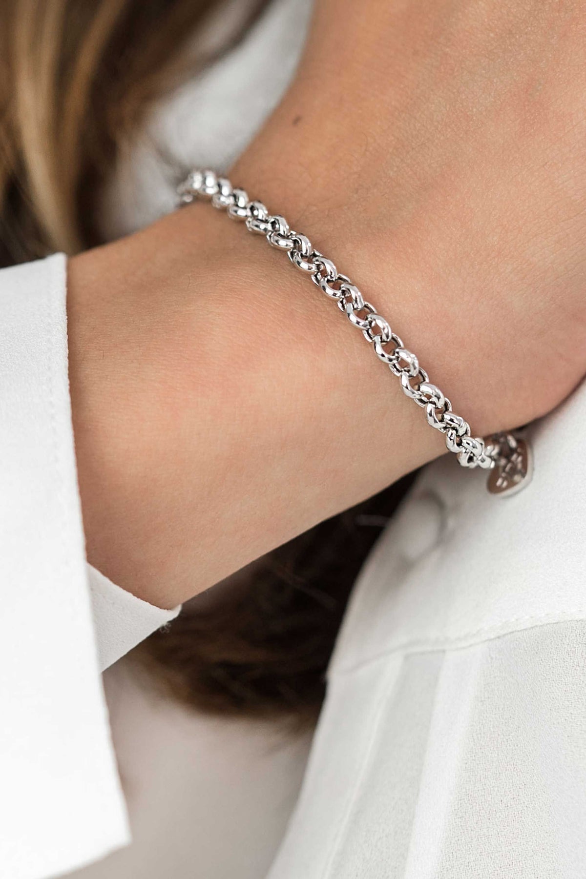 Een close-up toont een pols versierd met de Zinzi Armband Zilver Zia1911, met gevlochten kettingen en een bungelende bedel. De persoon draagt een wit shirt.