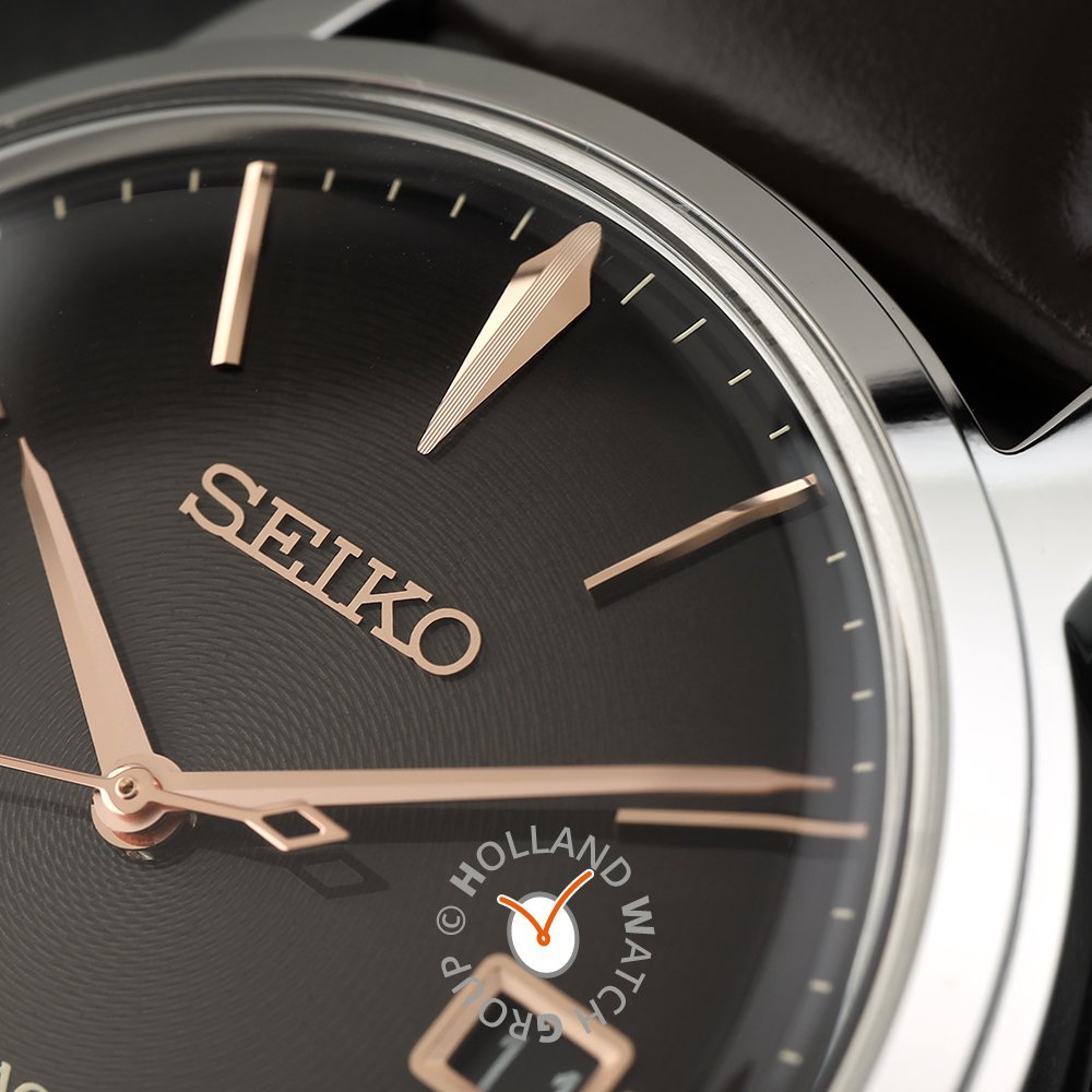 Close-up van het Seiko Presage heren horloge SRPJ17J1, met een zwarte wijzerplaat met roségouden wijzers en uurmarkeringen. Zilveren behuizing, automatisch uurwerk voor precisie en Hardlex mineraalglas voor duurzaamheid. Seiko wordt prominent weergegeven met het Holland Watch Group-logo in het midden.