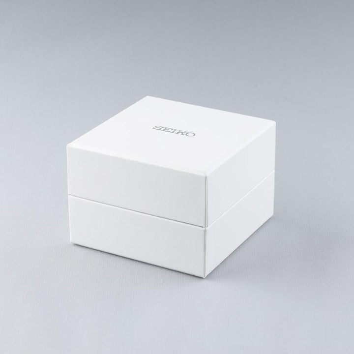 Een witte rechthoekige doos met Seiko in zilveren letters staat op een glad grijs oppervlak. Het eenvoudige, elegante ontwerp suggereert de robuuste betrouwbaarheid van het Seiko heren horloge SUR341P1 binnenin, beschermd door prachtig saffierglas.