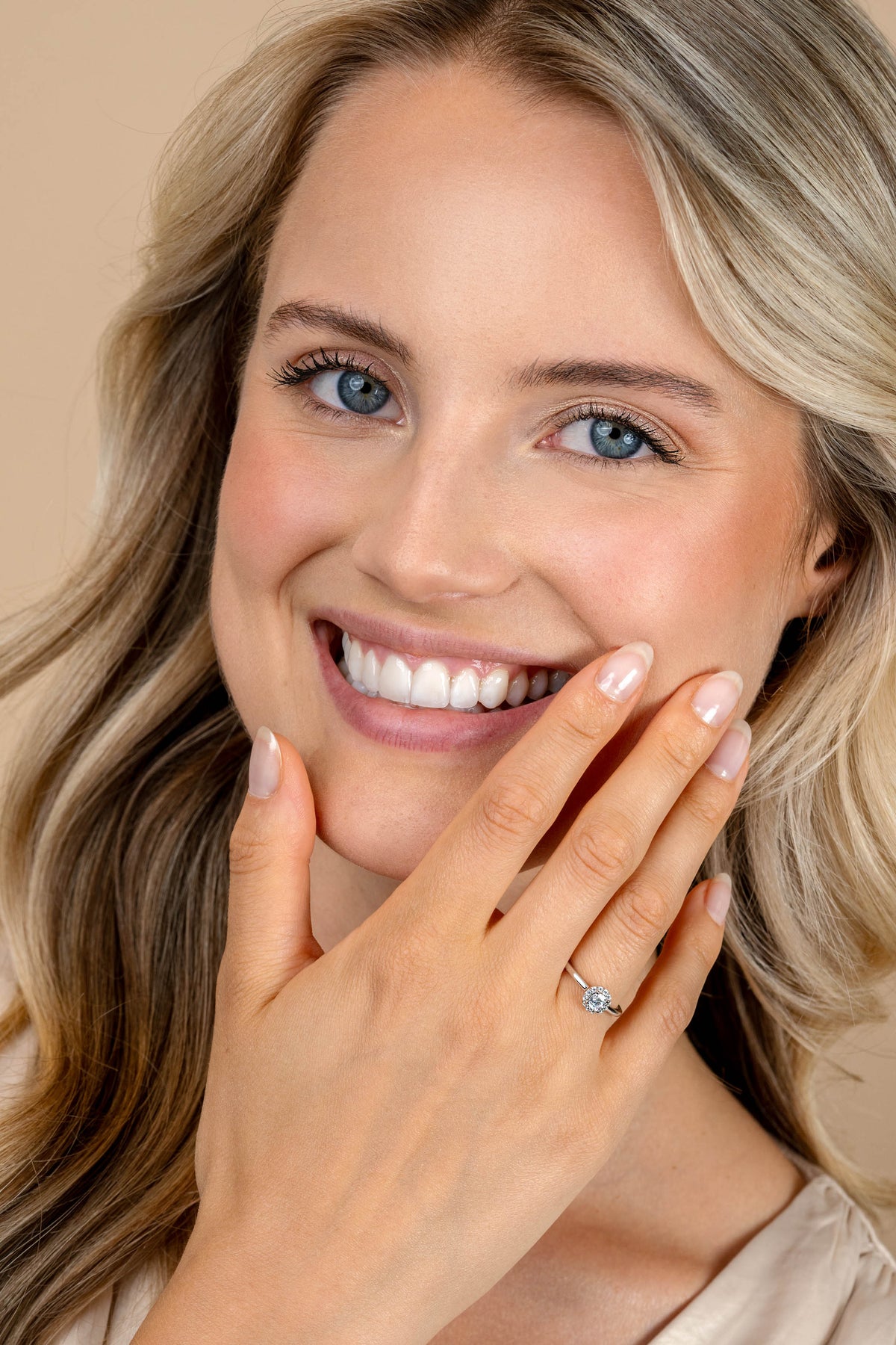 Een lachende blonde vrouw pronkt met de zilveren Zinzi Ring ZIR2697 aan haar linkerhand. Ze heeft een heldere huid, blauwe ogen, natuurlijke make-up en draagt een licht topje tegen een beige achtergrond.