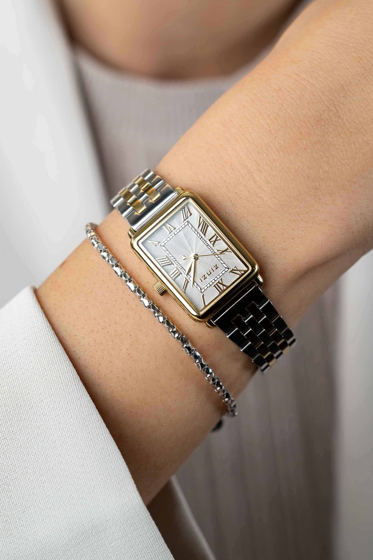 Een close-up van een pols met het Zinzi Geelgoudkleurig Horloge Staal Ziw1907, een stijlvol horloge van Zinzi met een gouden tint, gecombineerd met een fijne schakelarmband en een witte huls die gedeeltelijk zichtbaar is.