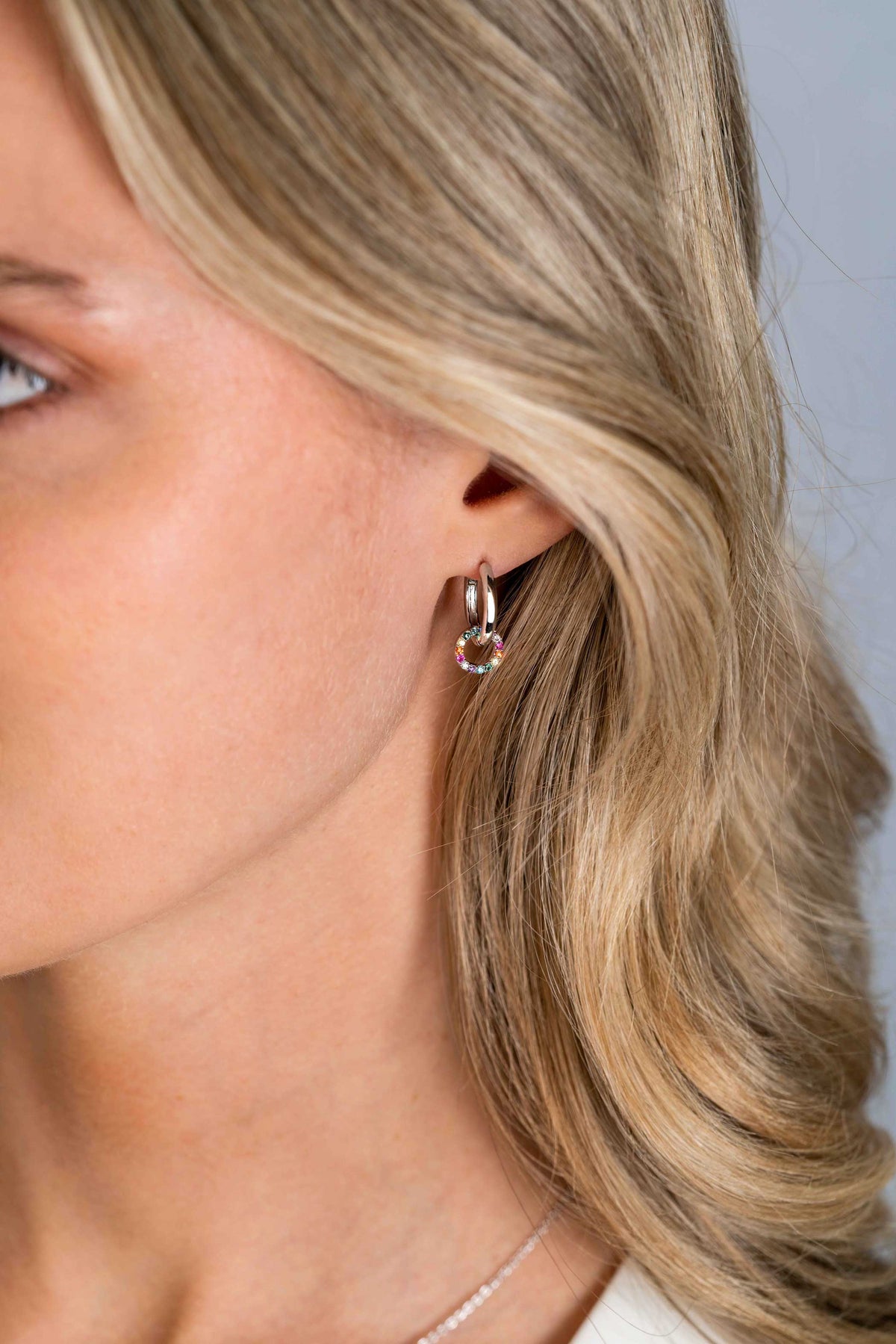 Close-up van een vrouw met blond golvend haar, die de Zinzi Oorbellen Zilver Zich2170Z oorbel draagt, met een hangende edelsteen, tegen een neutrale achtergrond. Alleen de linkerkant van haar gezicht en nek zijn zichtbaar.