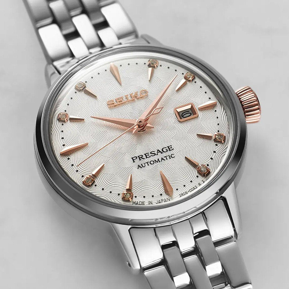 Close-up van het Seiko Presage dameshorloge SRE009J1 met een automatisch uurwerk in zilver en roségoud, met een gestructureerde witte wijzerplaat, roségouden wijzers en uurmarkeringen, een datumweergave op 3 uur, alles beschermd door Hardlex mineraalglas op een metalen band.